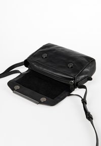 Zwarte leren crossbody tas met twee drukknoopsluitingen, ritscompartiment, zachte suède voering en een geweven banddetail.