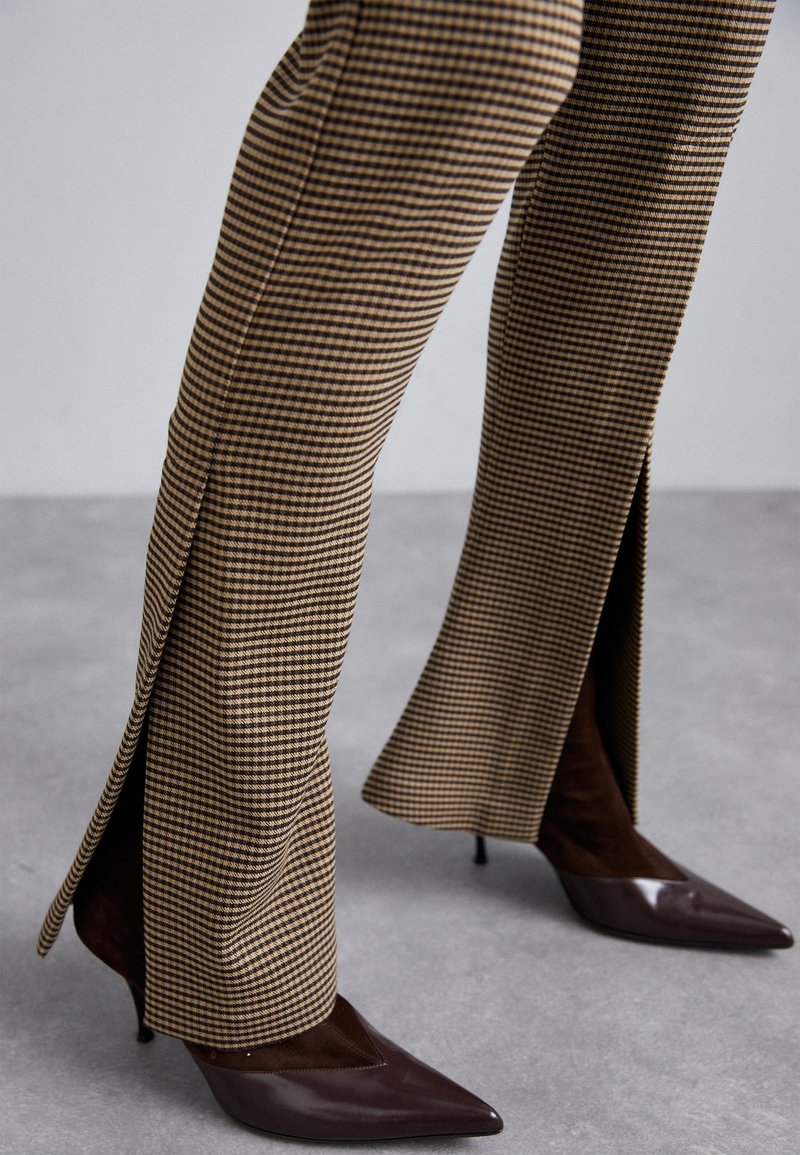 Brown plaid flared trousers with side slits and high-heeled pointed-toe shoes in dark brown. Textured fabric with distinct check pattern.