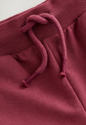 Burgunderfarbene Jogginghosen mit geripptem Bund, geflochtenem Kordelzug und weichem, strukturiertem Stoff. Nahaufnahme der Detailnaht.