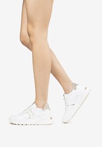 Sneaker bianco con materiali in tessuto e sintetici, dotata di un tallone imbottito, chiusura con lacci, dettagli argentati e suola testurizzata.