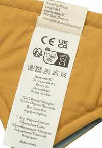 Cotton blend care label on a mustard background, featuring washing instructions, material information, and manufacturer details in multiple languages.