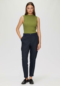 Groene geribbelde mouwloze top gecombineerd met strakke marineblauwe broek, met knoopsluiting en opgerolde mouwen, gedragen met zwarte instappers.