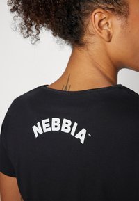 Crna majica od mekog materijala, s okruglim izrezom i bijelim logotipom "NEBBIA" otisnutim u luku na leđima.