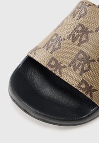 Sandale flip-flop de culoare cămilă cu partea superioară texturată, având un model de logo maro închis. Talpa este neagră și ușor rotunjită, cu un finisaj neted.