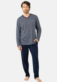 Haut à manches longues à pois blancs sur fond marine avec un décolleté en V et une poche, associé à un pantalon de pyjama uni marine. Coupe douce et décontractée.