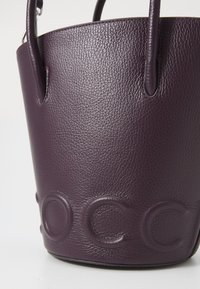 Purple leather bucket bag with pebbled texture, featuring two round handles and embossed logo detail at the bottom.