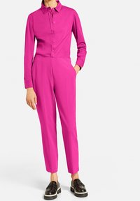 Tuta fucsia con maniche lunghe, patta con bottoni e gambe affusolate. Realizzata in un tessuto liscio; presenta tasche laterali e colletto.
