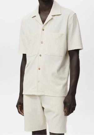 Homme portant une chemise beige clair à manches courtes avec deux poches poitrine et un short assorti.