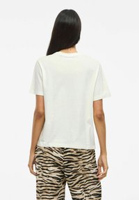 Vit kortärmad t-shirt med rund halsringning, visad bakifrån, i kombination med byxor i tigerhållsmönster med svarta och bruna mönster.