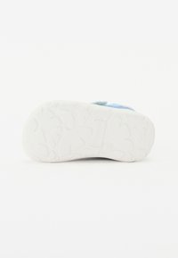 Zapato infantil con suela de goma blanca que presenta patrones de agarre texturizados, parte superior de textil azul y correa ajustable de velcro.