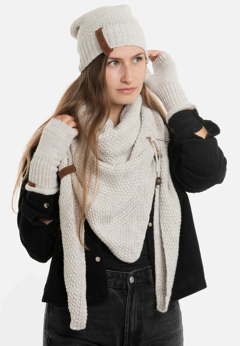 Lichtgrijze gebreide beanie, bijpassende sjaal en vingerloze handschoenen met leren accenten. Gelaagd ribbelpatroon en gezellige textuur.