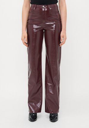 Persoon in hoge taille, donker bordeaux glanzende wijde broek met voorzakken, gecombineerd met zwarte patentleren schoenen en een zwart topje.