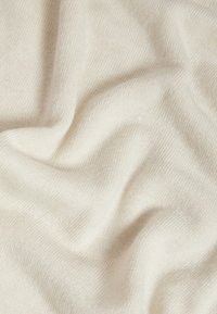 Tessuto a maglia di un leggero beige con una consistenza morbida e liscia, caratterizzato da sottili motivi intrecciati e onde create dalla caduta.