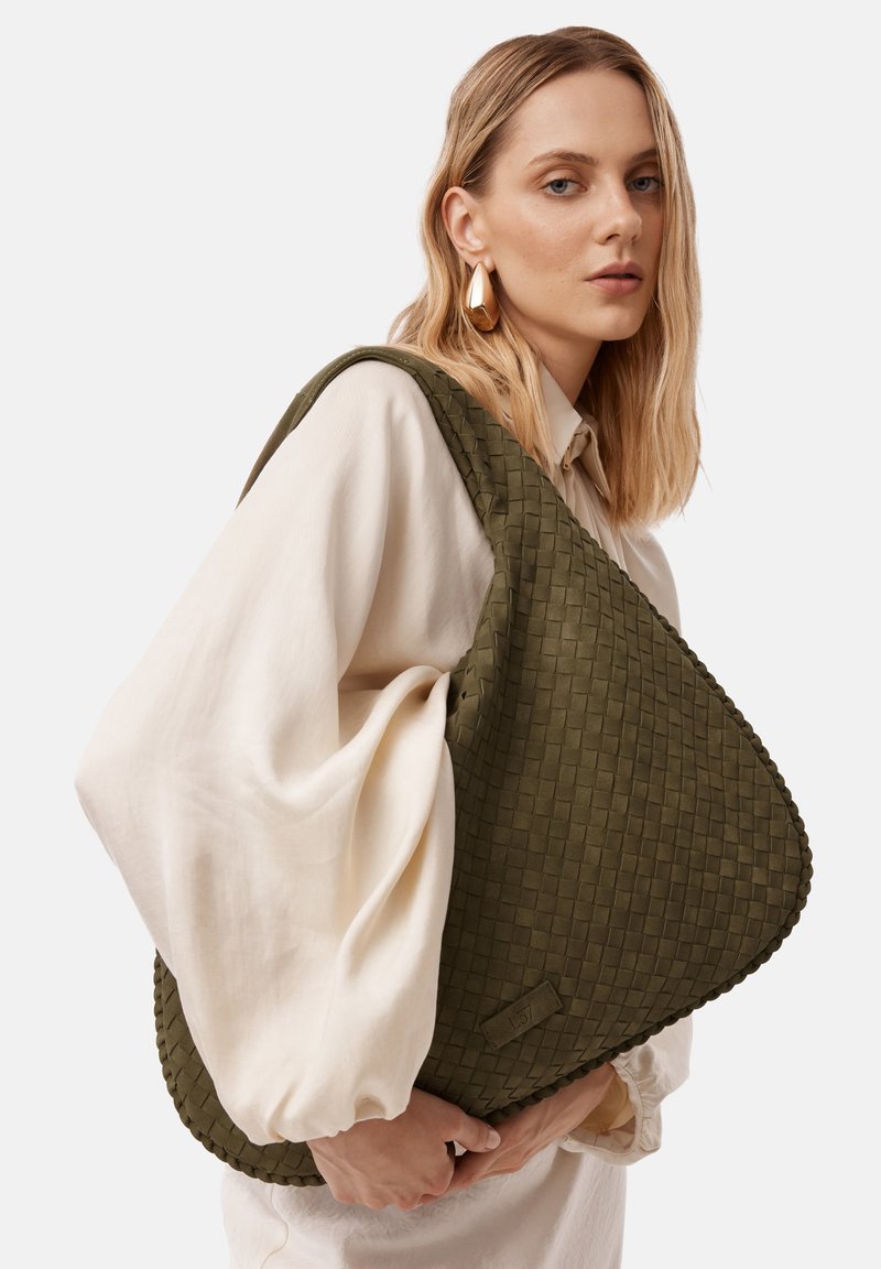 Sac à épaule tissé vert avec une forme triangulaire, une surface texturée et un bord lisse. Le sac présente un matériel de quincaillerie minimal et un logo discret.