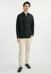 Czarna koszula z guzikami, wykonana z lekkiego materiału, w połączeniu z kremowymi spodniami i czarnymi butami na wsuwkę. Gładka faktura, dopasowany krój.