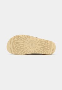 Rubberen schoenzool in beige met een gestructureerd patroon. Bevat een centraal logo en hoekige ontwerpen voor grip en tractie.