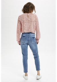 Crochet-style pink blouse with long, puffed sleeves and back keyhole detail, paired with light blue jeans featuring back pockets and a slim fit.
