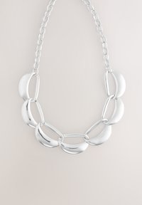 Collier en chaîne argentée composé de maillons incurvés et allongés avec une finition polie, alternant les formes pour une apparence dynamique et texturée.