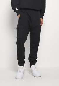 Svarta joggerbyxor med elastisk midja, två sidofickor och två cargofickor. Slätt tyg med ribbade muddar, kombinerat med vita sneakers.