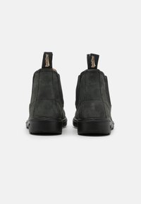 Botas chelsea de ante negro con paneles laterales elásticos, suela de goma plana y lengüetas para ponerlas y quitarlas fácilmente. Textura suave y diseño minimalista.