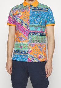 Kortärmad polo med en livfull flerfärgad lapptäckedesign med blommönster och paisleymönster. Orange krage och kantband. Tillverkad i bomull.