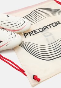 White soccer cleats with black and red accents, paired with a drawstring bag featuring a wavy black design and "PREDATOR" label. Red cords.