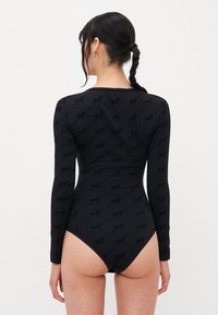 Černý body s dlouhými rukávy, který se vyznačuje jemným vzorem s logem po celém povrchu, slim fit střih a designem s vykrojeným zadním výstřihem bez viditelných zapínání.