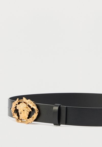Čierny kožený opasok s prackou v štýle zlatej medaily, ktorá má detailný motív tváre a vavrínového venca. Jednoduchá a elegantná konštrukcia.
