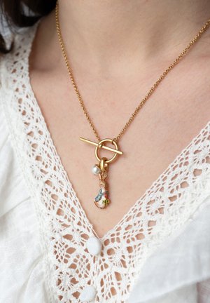 Collana in oro con chiusura a moschettone, caratterizzata da un pendant multicolore con una figura decorativa e un accento di perla. Top in pizzo testurizzato sotto.