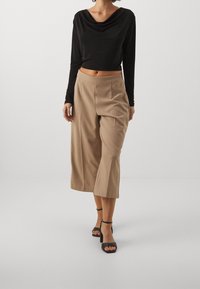 Schwarzes Longsleeve-Oberteil mit drapiertem Ausschnitt, kombiniert mit beigefarbenen, weit geschnittenen Culottes. Modell trägt schwarze Blockabsatzsandalen.