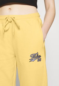 Gelbe Sweatpants mit elastischem Bund, Kordelzug, Seitentaschen und gesticktem "Fabu 05"-Logo in Blau und Schwarz. Weich im Stoff.
