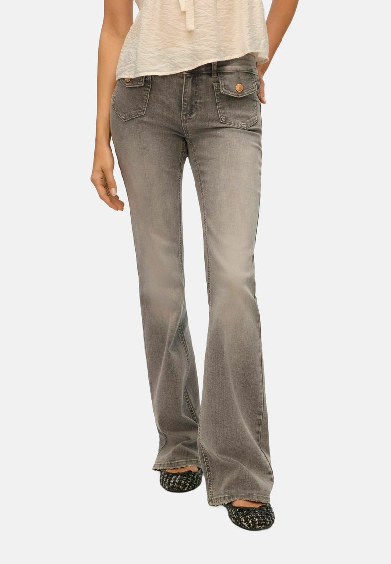 Jean grise évasée en denim avec une finition légèrement délavée, comportant des poches avant et des accents en métal de couleur cuivrée.