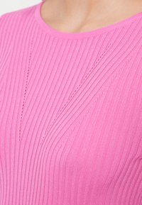 Ροζ εφαρμοστό ριμπ πουλόβερ με στρογγυλή λαιμόκοψη και διαγώνια πλέξη στο στήθος. Μαλακή υφή με λείο φινίρισμα.