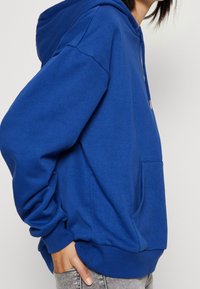 Felpa blu con cappuccio, tasca a marsupio, polsini e orlo a costine, realizzata in un tessuto morbido con una vestibilità comoda.