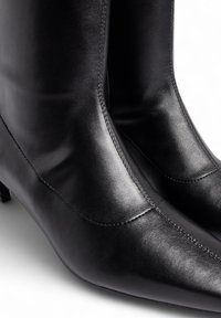 Botas de tobillo negras de cuero con punta afilada, que presentan una textura suave, costuras mínimas y tacón bajo cuadrado.