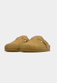 Καφέ καστόρινες κλειστές παντόφλες με στρογγυλεμένη μύτη, ρυθμιζόμενο λουράκι με αγκράφα και υφασμένο πέλμα. Μαλακό υλικό και μινιμαλιστικός σχεδιασμός.