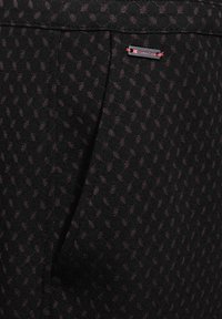 Černá látka s jemným vzorem v tmavě fialové barvě. Obsahuje dekorativní štítek s červenými akcenty. Hladká textura. Ušitý design s kapsami.