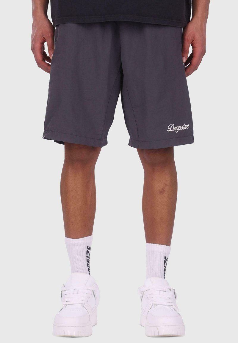 Grå shorts lavet af letvægtsstof med en afslappet pasform, der har et broderet "Dogsize"-logo. Parret med hvide sneakers og sokker.