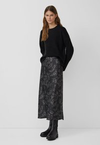 Zwarte gebreide trui, grijze gebloemde satijnen rok met een vloeiende design, en zwarte enkellaarsjes met een chunky zool. Over het algemeen een soepele textuur.