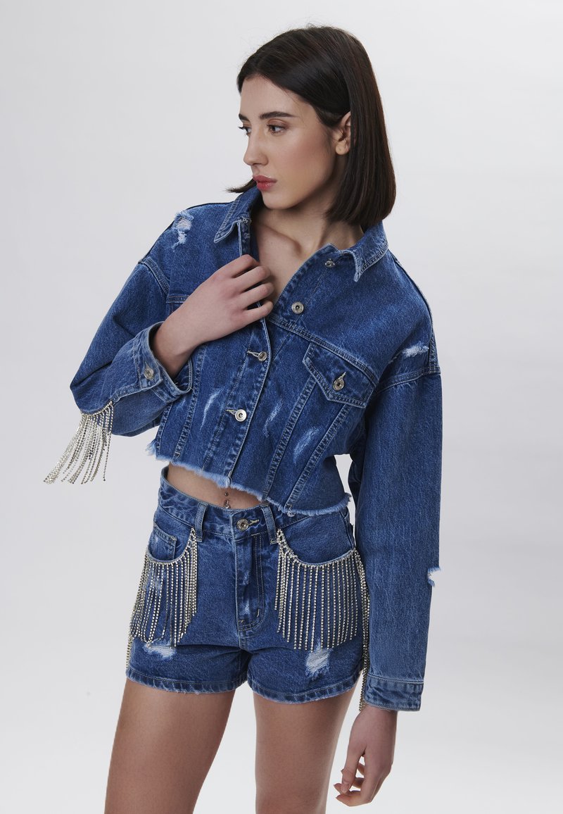 Veste en denim courte avec des bords effilochés et des franges en perles argentées sur les manches, assortie à un short taille haute avec des accents de poches en perles.