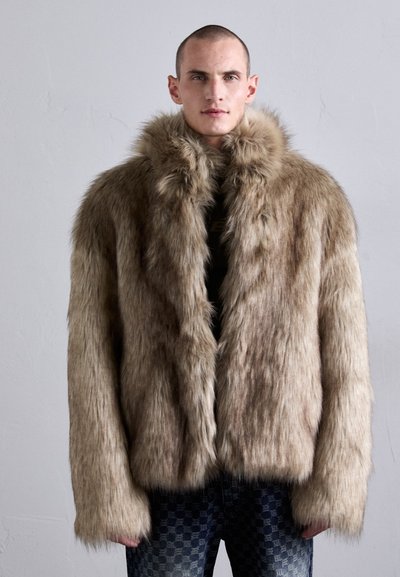 Manteau en fausse fourrure brun clair avec une texture dense et douce. Doté d'un large col, de manches longues et d'une coupe décontractée, associé à un denim à motifs.