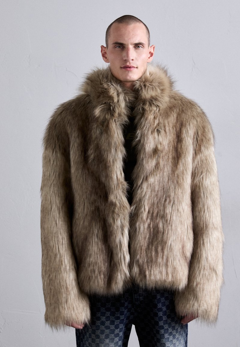 Faux fur frakke i lys brun med en tæt, blød tekstur. Har en bred krave, lange ærmer og en afslappet pasform, som er parret med mønstret denim.