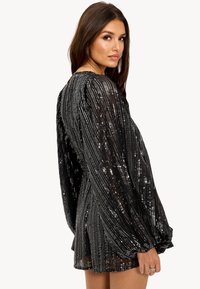 Robe mini noire avec de longues manches bouffantes. Fabriquée dans un tissu texturé orné de sequins brillants disposés en motif vertical.
