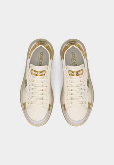 Λευκά και χρυσά sneakers χαμηλού ύψους με κορδόνια, με τη μάρκα «roberto cavalli» στην γλώσσα και στην εσωτερική σόλα, απεικονισμένα από πάνω σε απλό φόντο.
