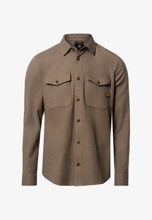 Chemise marron cintrée à manches longues avec devant boutonné, deux poches poitrine à rabat, et une petite étiquette de marque jaune sur la poche droite.