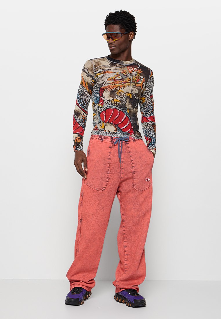 Langärmliges Hemd mit Grafikdruck von Drachen und Mustern, kombiniert mit lockeren, ausgebleichten roten Hosen, die über Seitentaschen und einen Kordelzugbund verfügen.