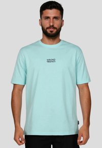 Světle modré tričko s krátkým rukávem vyrobené z bavlny, s centrálním černým logem "WRONG FRIENDS". Jednoduchý design s kulatým výstřihem.
