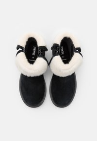 Botines de ante negros con un suave collar blanco, superficie texturizada, puntera redondeada y detalles de cordones en la parte frontal. El interior tiene etiquetado de la marca.