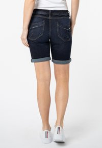 Donkerdenim shorts met opgerolde zomen, voorzien van twee achterzakken en subtiele stiksels. Gepaarde met witte sneakers.