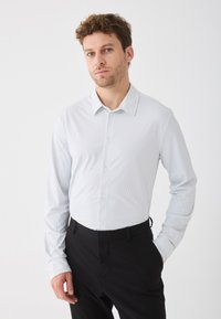 Camicia a maniche lunghe a righe azzurro chiaro con colletto a punta, pattina con bottoni e maniche con polsini, abbinata a pantaloni neri.